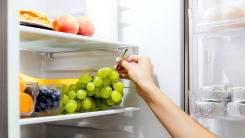 Hand reaching into a refrigerator to grab a bunch of grapes