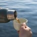 Person's hand pouring wine out of a thermos and into a mug.