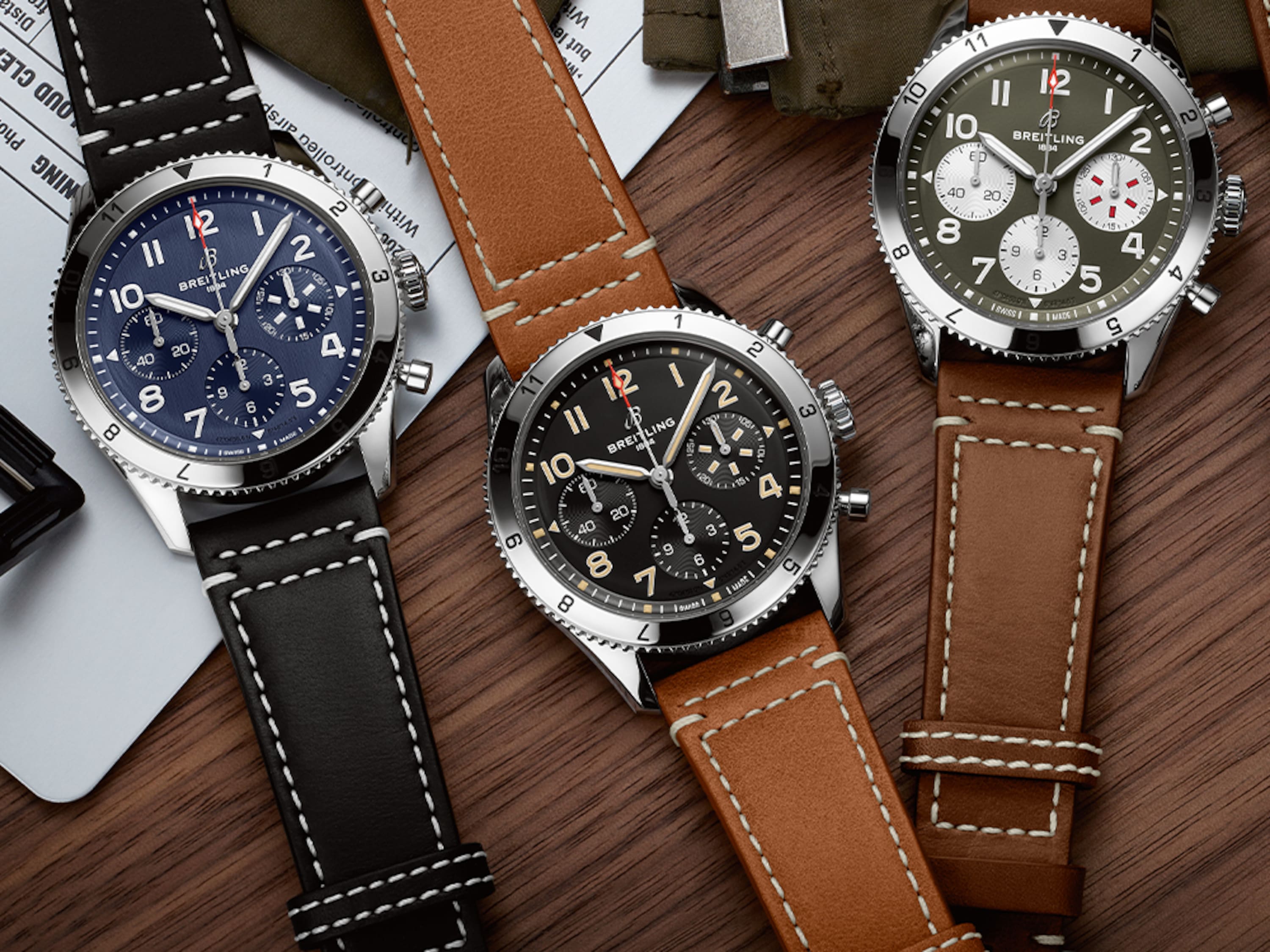 Three Classic AVI with different colored, dark leather straps on a dark brown table.