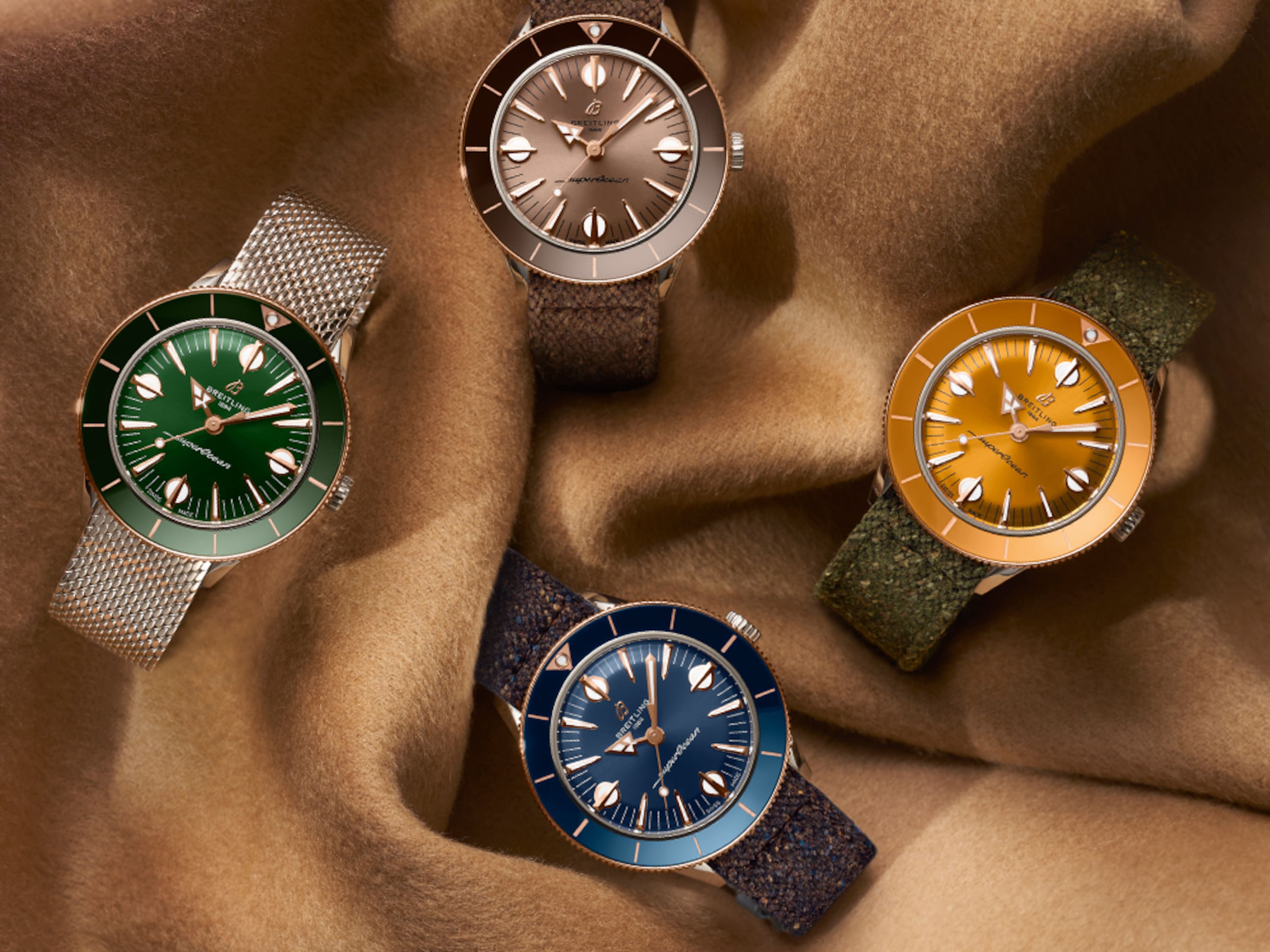 Four different colored Superocean Heritage watches lie on a brown cloth.
