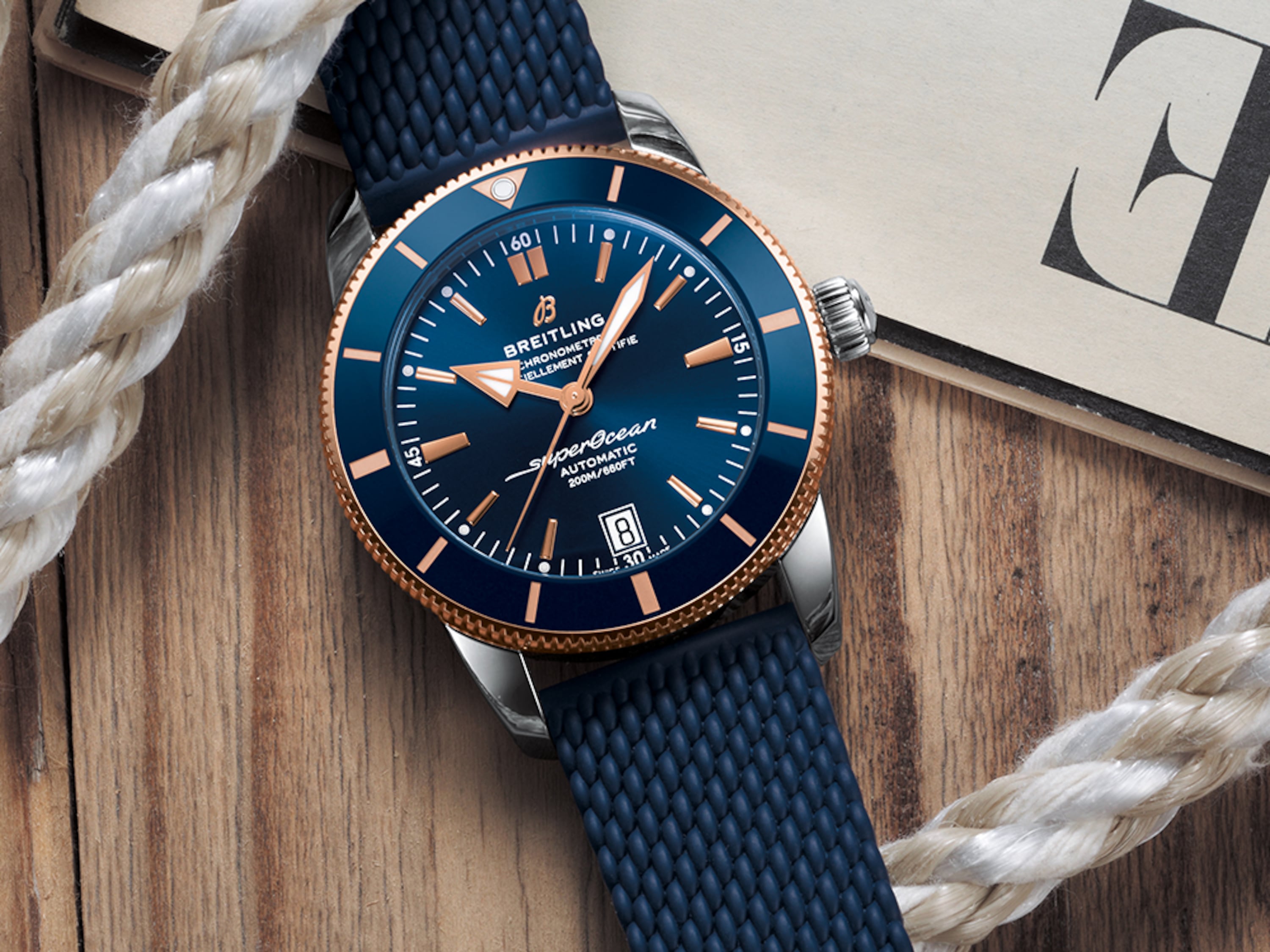 A dark blue Superocean Heritage lies on a table with a magazine and a white rope.